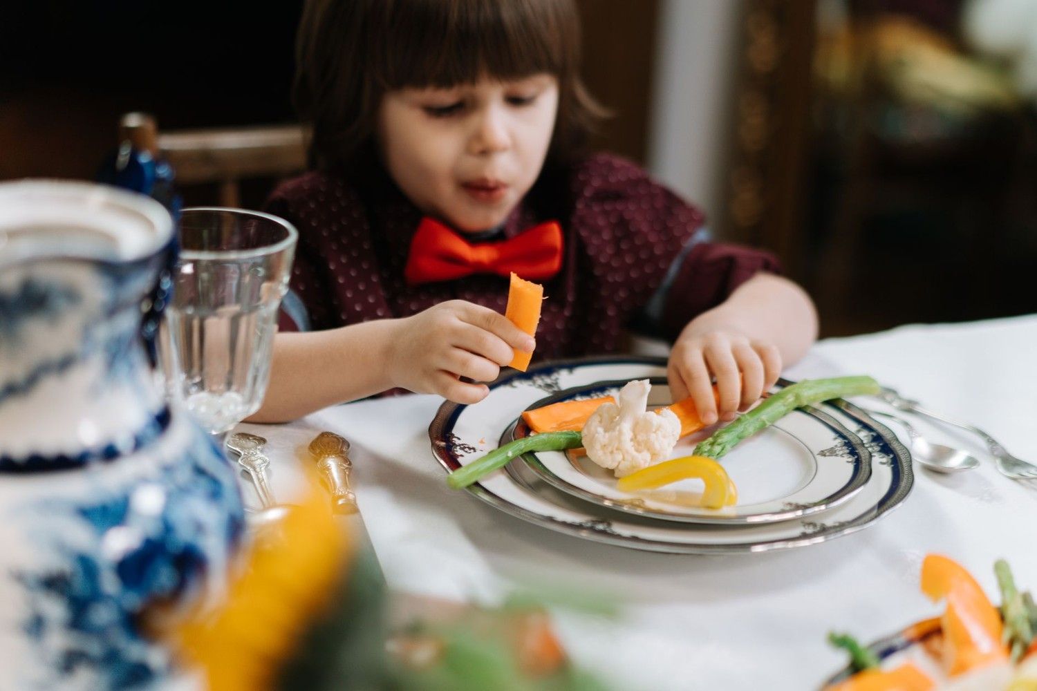 幼童坐在餐桌前用手拿紅蘿蔔與蘆筍吃飯